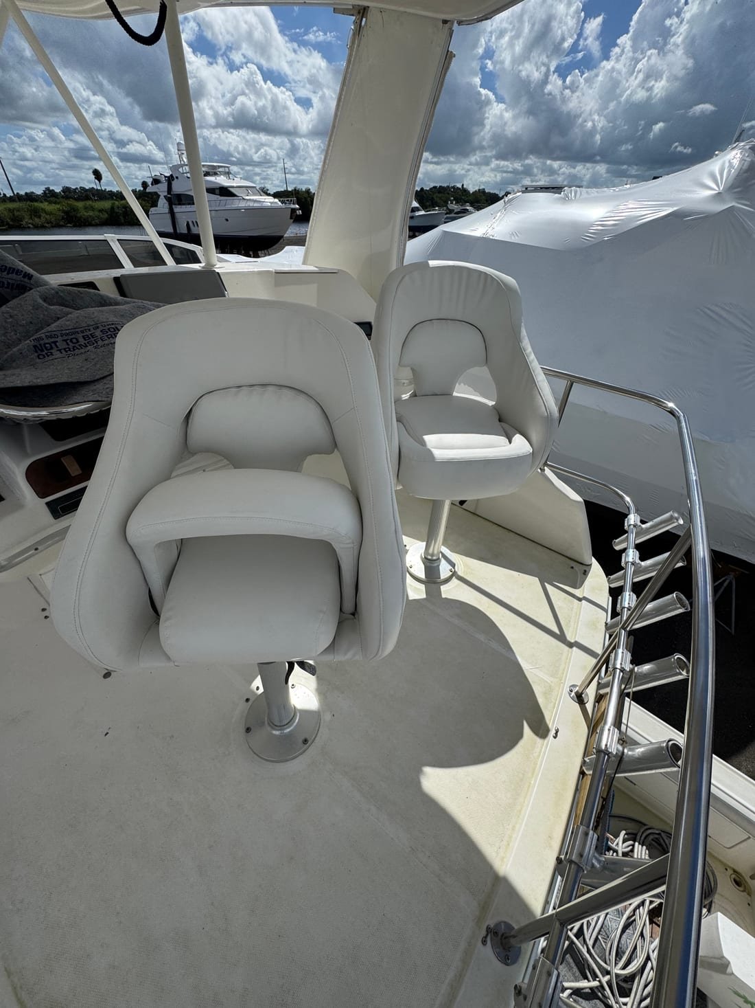 Two white upholstered helm chairs on a flybridge under an overcast sky