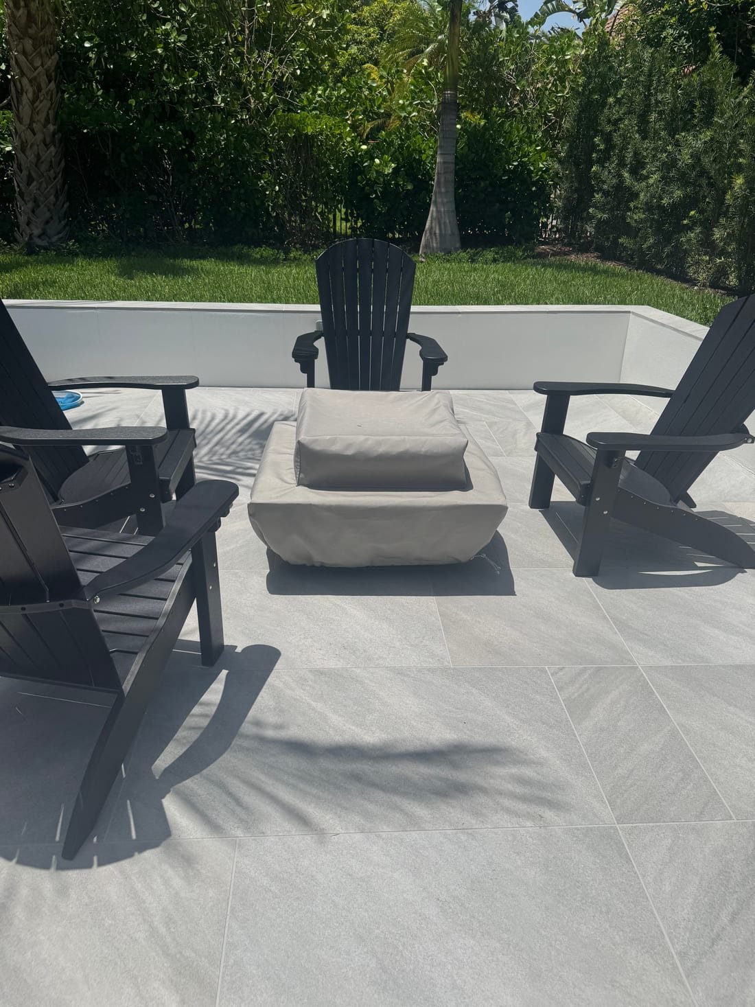 A cushioned outdoor ottoman between black Adirondack chairs on a paver patio