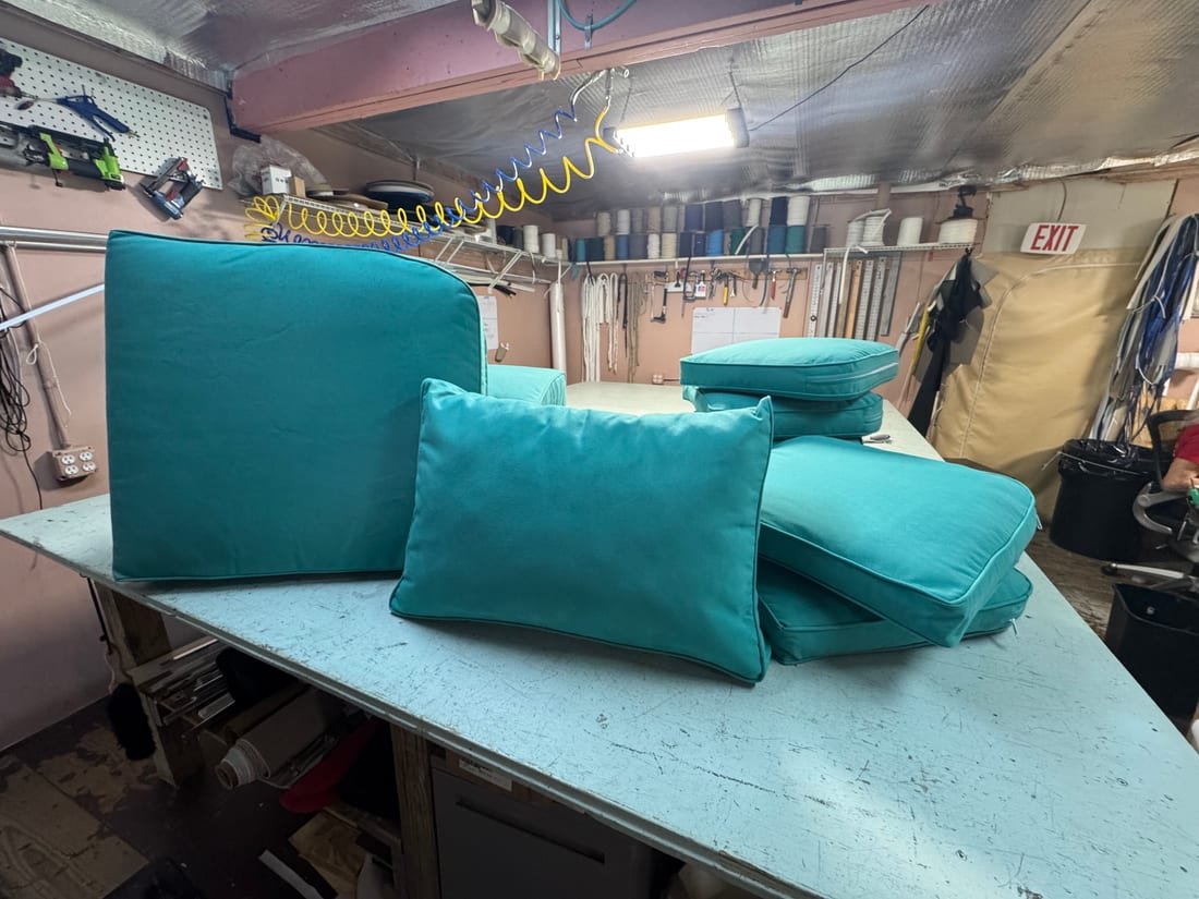 A set of teal marine cushions and bolsters stacked on a workshop table